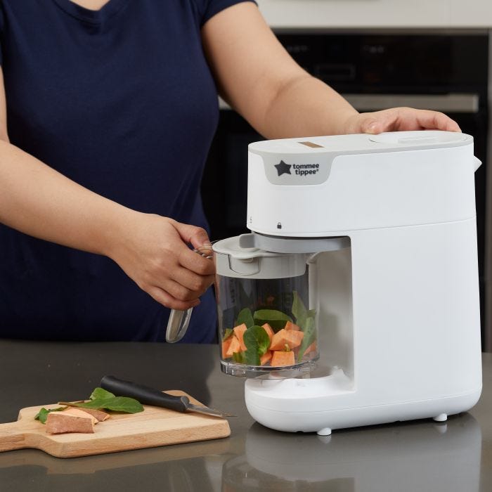 Woman placing veggie-filled basket into the food maker to steam and blend