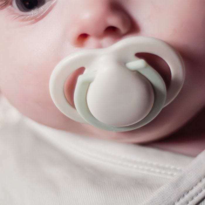 Close up of cream and green soother in baby’s mouth