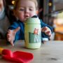 Toddler reaching for Superstar Sipper Training Cup, green on tabletop