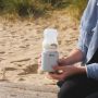 Woman holding LetsGo bottle warmer with upside down baby bottle on top while at the beach
