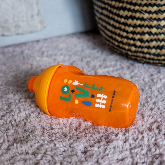 Orange sippee cup lying flat on a carpet