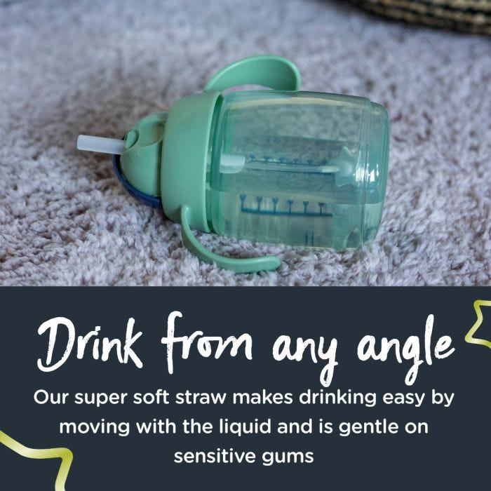 Green weighted straw cup lying flat on a carpet with text about drinking from any angle