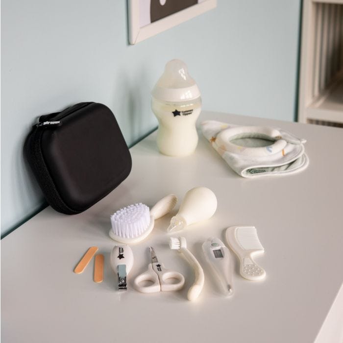 Contenu du kit de soin sur une table blanche à côté d&apos;une mallette de voyage, un biberon et un bavoir d&apos;allaitement.