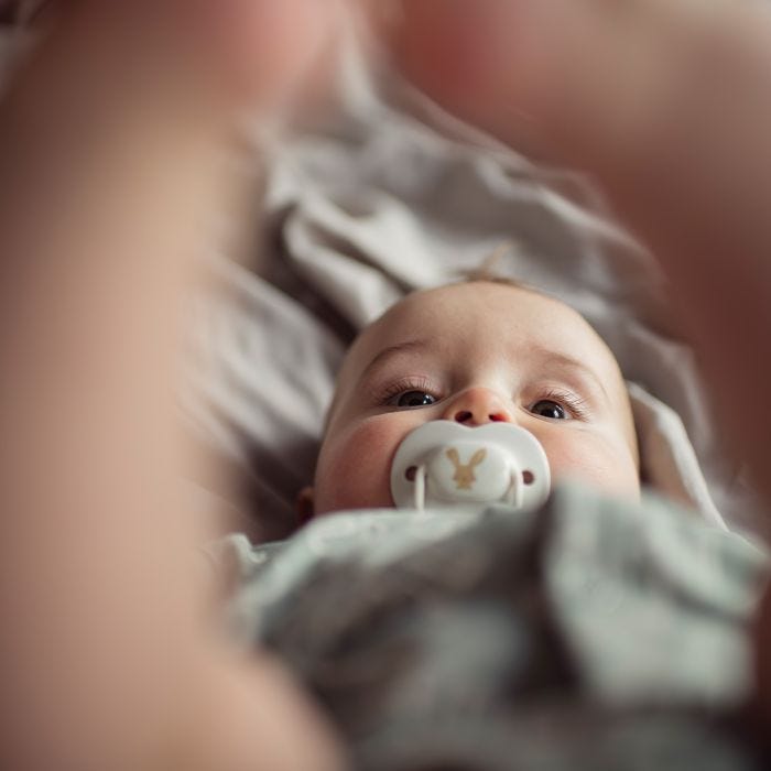 Baby with pacifier in mouth laying with there legs in the air