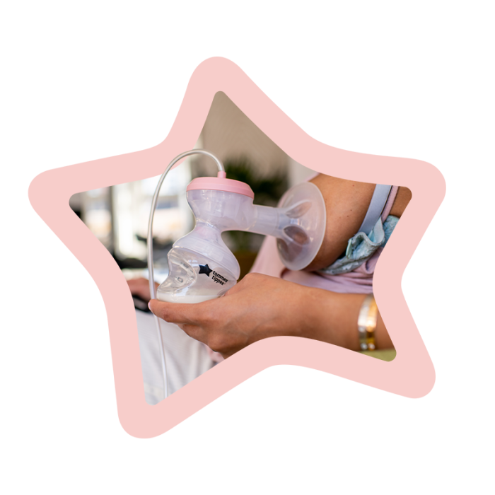 Woman using the single breast pump on one breast while sitting on the sofa surrounded by a pink star