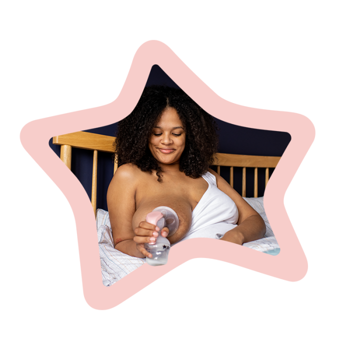 Woman sitting in bed while using a manual breast pump on her right breast surrounded by a pink star.