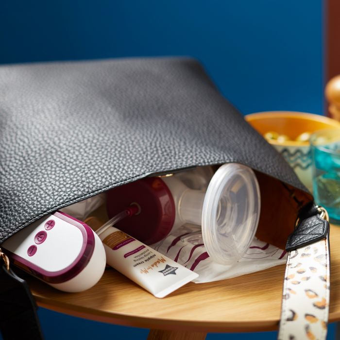 Handbag lying flat on a table with a breast pump and nipple cream peeping out