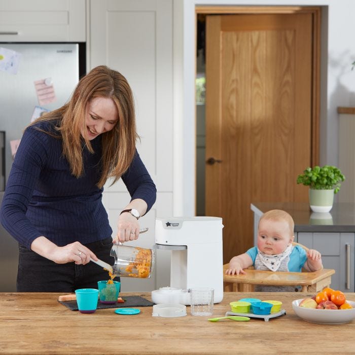Woman making puree for her baby who sits in a highchair next to her