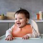 Toddler sitting in a highchair and wearing a roll’n’go bib