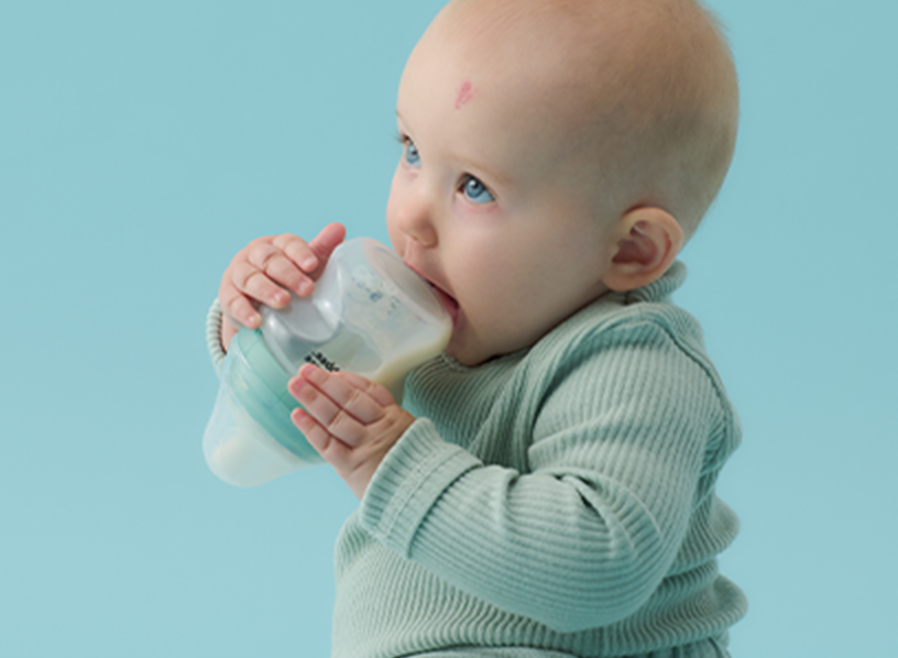 a baby holding an upside down Tommee Tippee bottle 