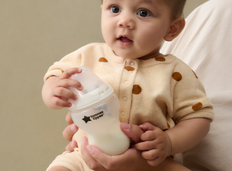 A baby holding a Tommee Tippee bottle 